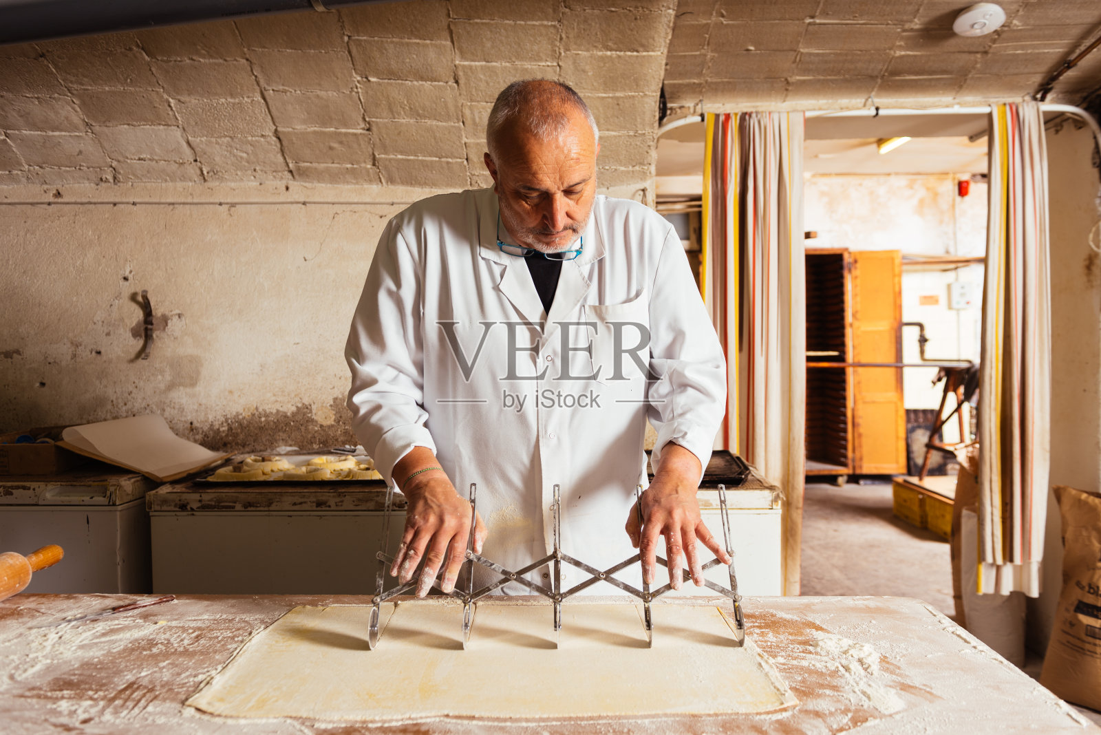 中年男子在厨房的桌子上用擀面刀切面团照片摄影图片