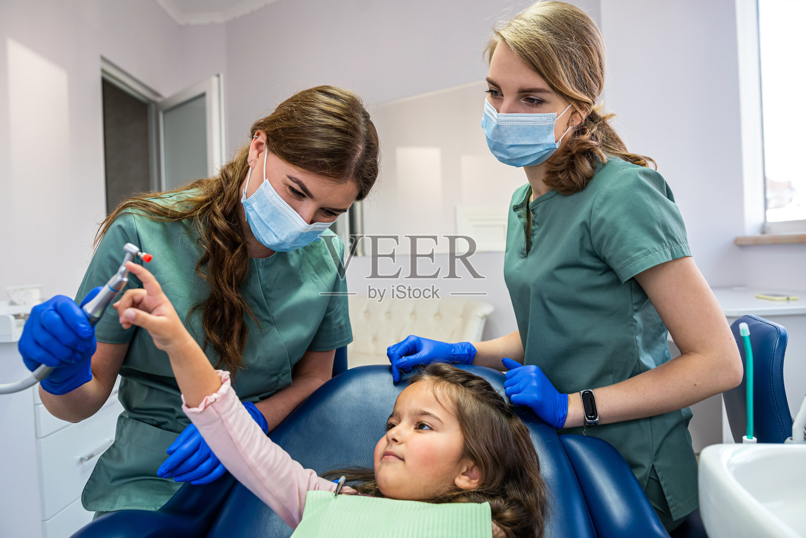 两个年轻漂亮的牙医女孩戴着口罩和手套为婴儿清洁口腔。照片摄影图片