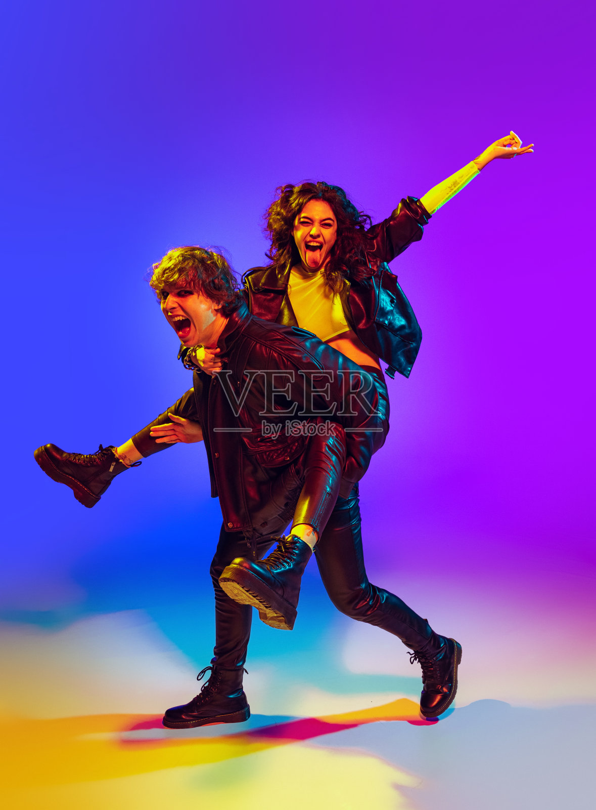 一对年轻的摇滚音乐家穿着黑色的皮衣，在霓虹灯下的蓝色背景下做着手势，大喊大叫，摆着姿势照片摄影图片