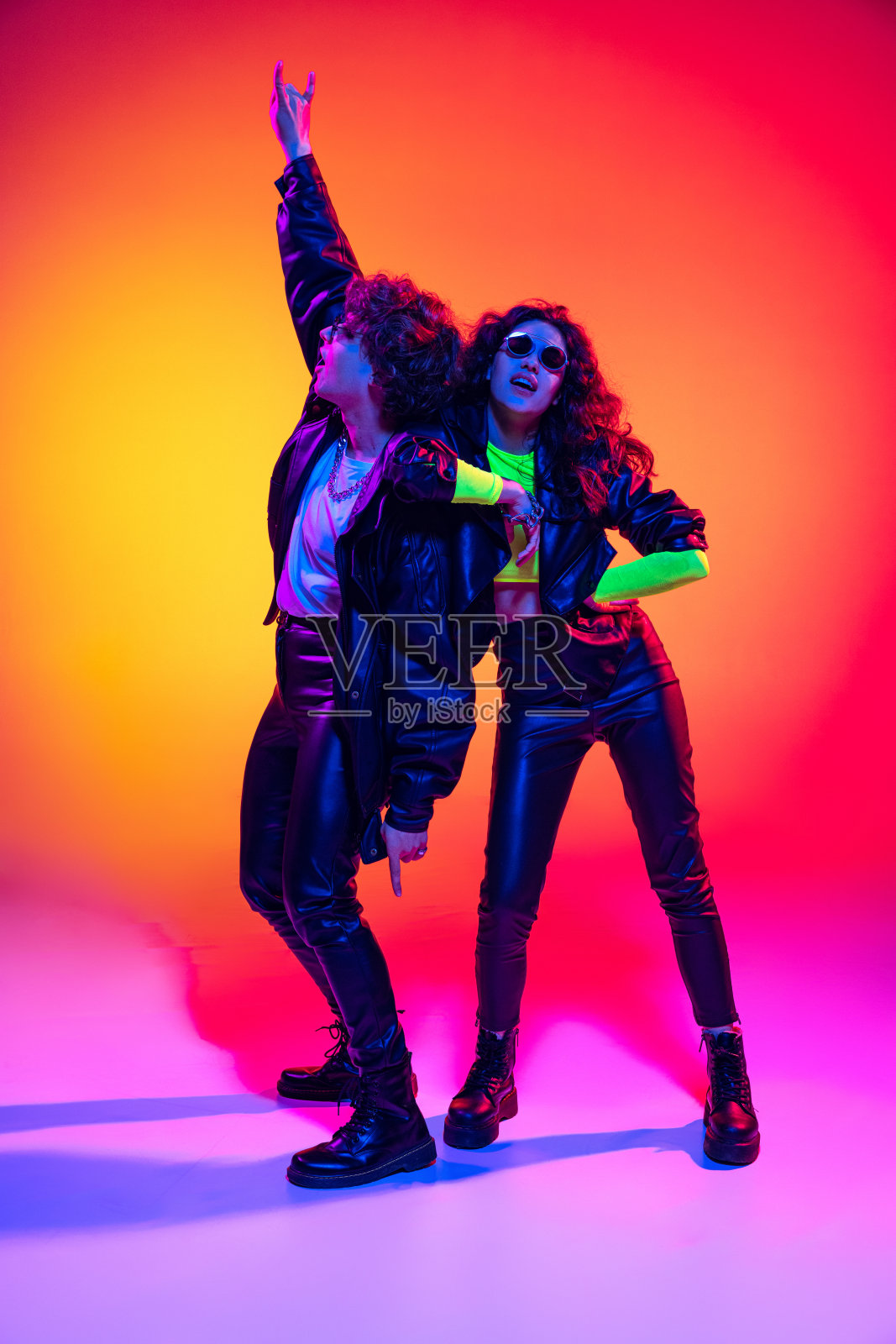 兴奋的年轻人和女孩在黑色皮衣玩，手势，喊叫和跳跃的霓虹灯下的黄红色背景照片摄影图片