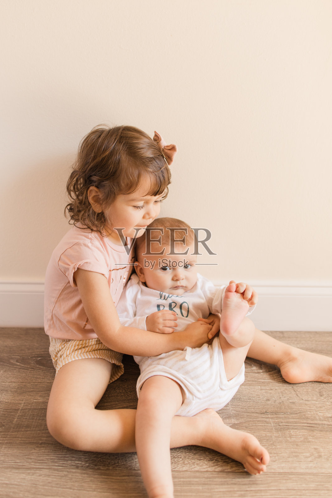 一个3岁的蹒跚学步的小女孩抱着她4个月大的弟弟，同时穿着“大姐姐”和“小弟弟”的衬衫照片摄影图片