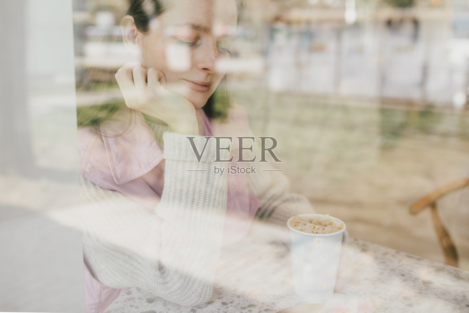 年轻女子坐在咖啡厅靠窗的地方，享受拿铁咖啡。照片摄影图片