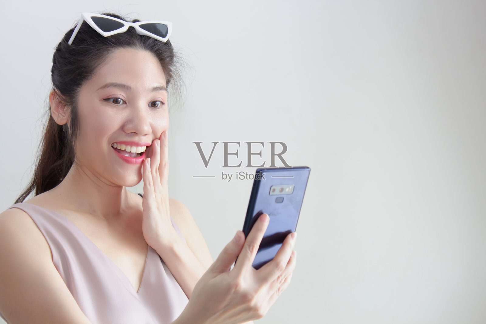 亚洲美女看着智能手机，举起手，触摸嘴唇，微笑，在聊天或网上购物或赢得彩票或赢得游戏的幸福和惊喜照片摄影图片