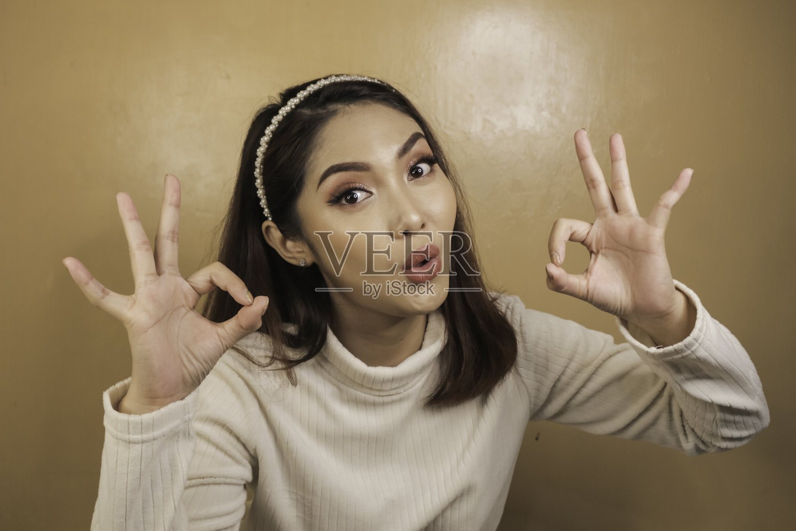 一名年轻的亚洲女性的震惊的脸，她的标志是“OK”，穿着白衬衫。广告的概念。照片摄影图片