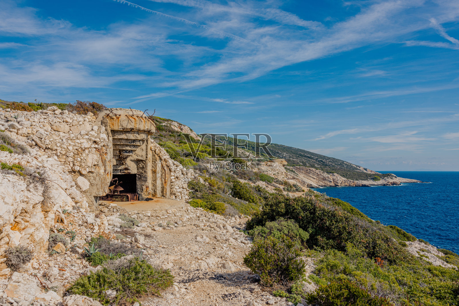 岛上一座山的山顶上有一个二战时期的旧地堡，地堡里有一个陈旧的棕色生锈的炮筒，背景是大海照片摄影图片