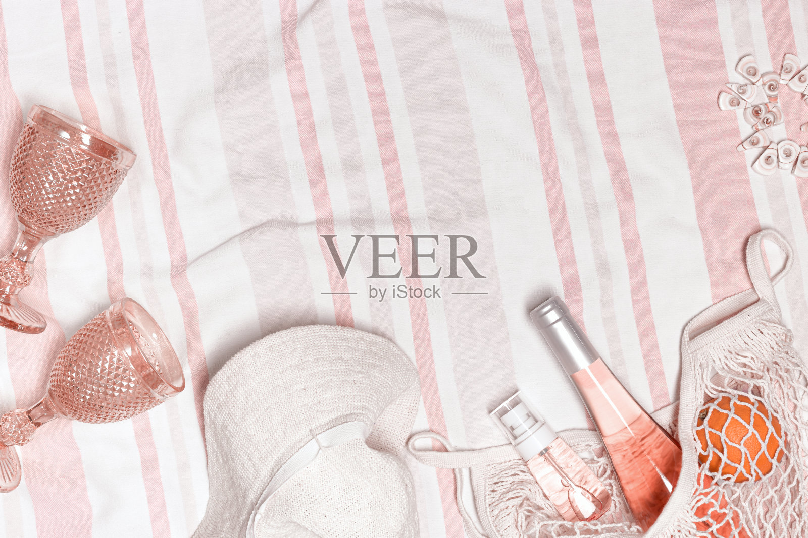 夏季生活方式平铺与太阳帽，化妆品产品，瓶玫瑰酒和两个酒杯，橙色水果在网袋上的海滩毛巾为背景。夏日海滩度假和聚会的概念照片摄影图片