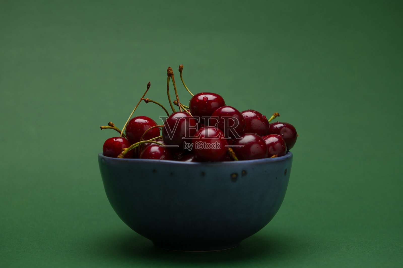 静物与一个成熟的有机甜樱桃浆果在深绿色背景的蓝色陶瓷碗。食品的背景照片摄影图片