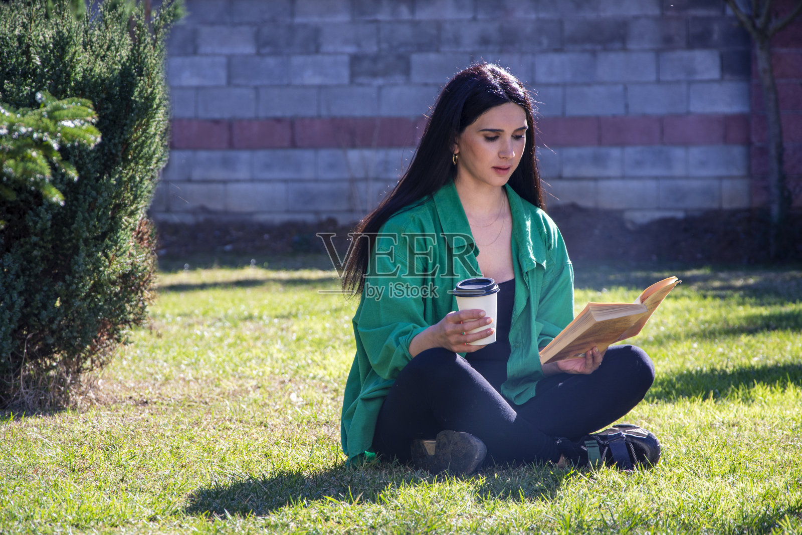 一位年轻女子正在户外的草地上喝着咖啡看书照片摄影图片