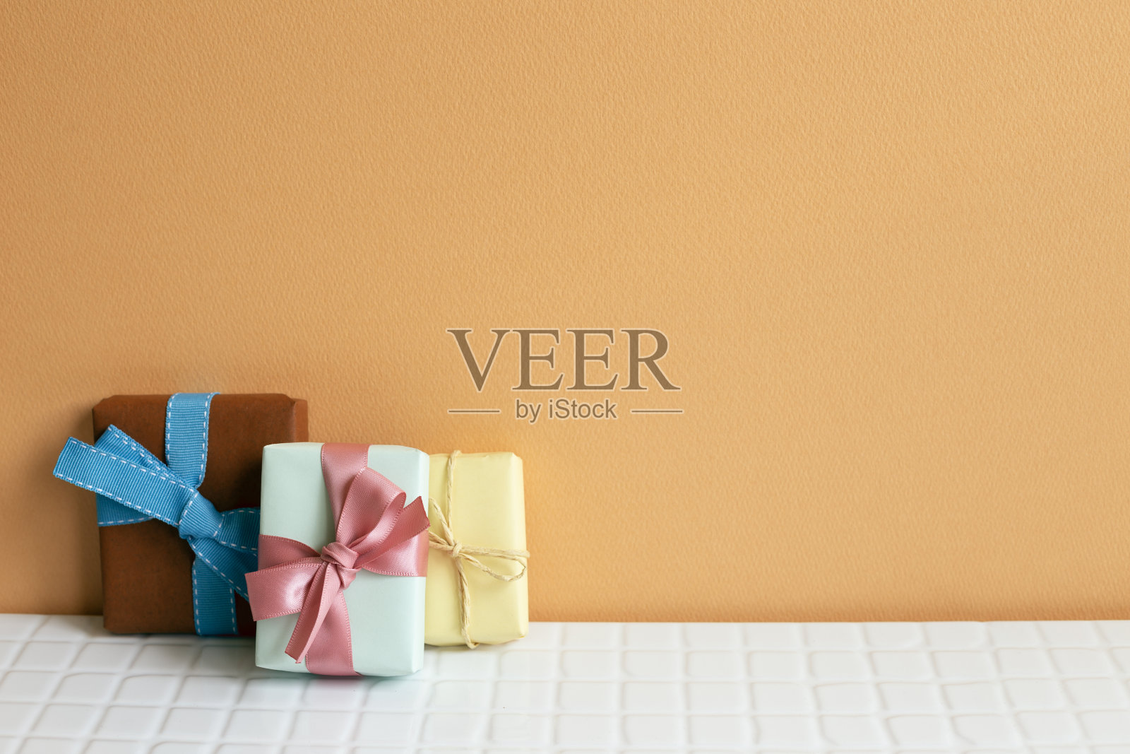 白色桌子上五颜六色的礼品盒。橙色的背景墙。本空间照片摄影图片