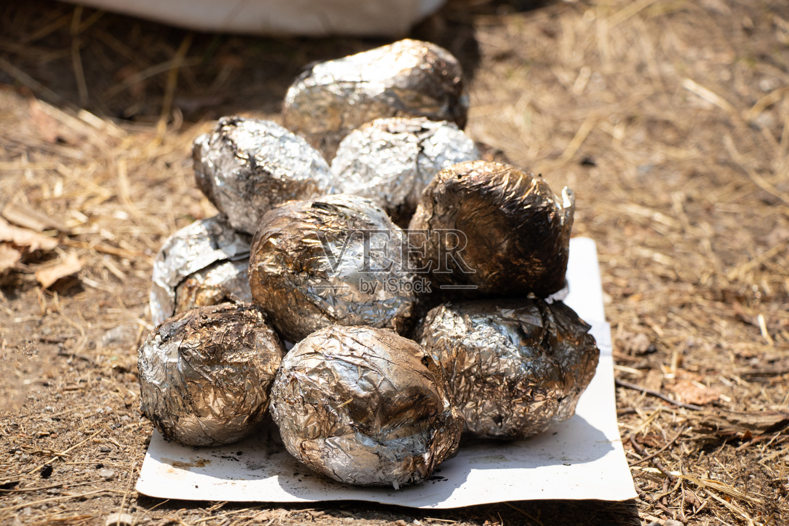 夏天野餐时，在炭火上烤制的锡箔土豆堆在纸上，堆在地上，烤架上的食物，午餐照片摄影图片