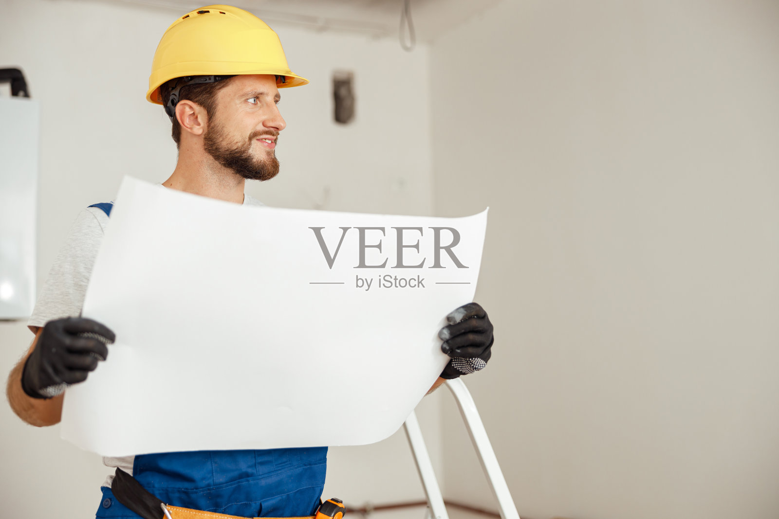 肖像深思建筑工人戴安全帽看向别处，而研究蓝图，站在新公寓照片摄影图片