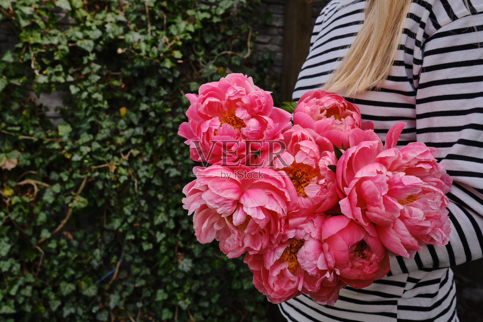 幸福的女人手里拿着粉红色的牡丹。花店女孩收集了一束牡丹。娇嫩的花是美丽的。一份节日礼物，春天心情。浪漫的惊喜照片摄影图片