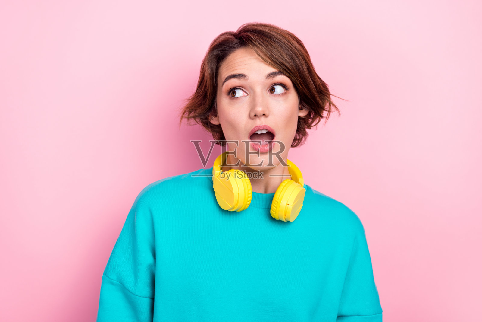 印象深刻的年轻女孩的肖像张开嘴凝视无语的空间挂脖子耳机孤立在粉红色的背景照片摄影图片