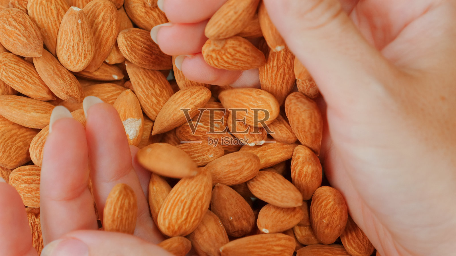 微距镜头的女人手拿着整个杏仁，一种美味和松脆的零食。照片摄影图片