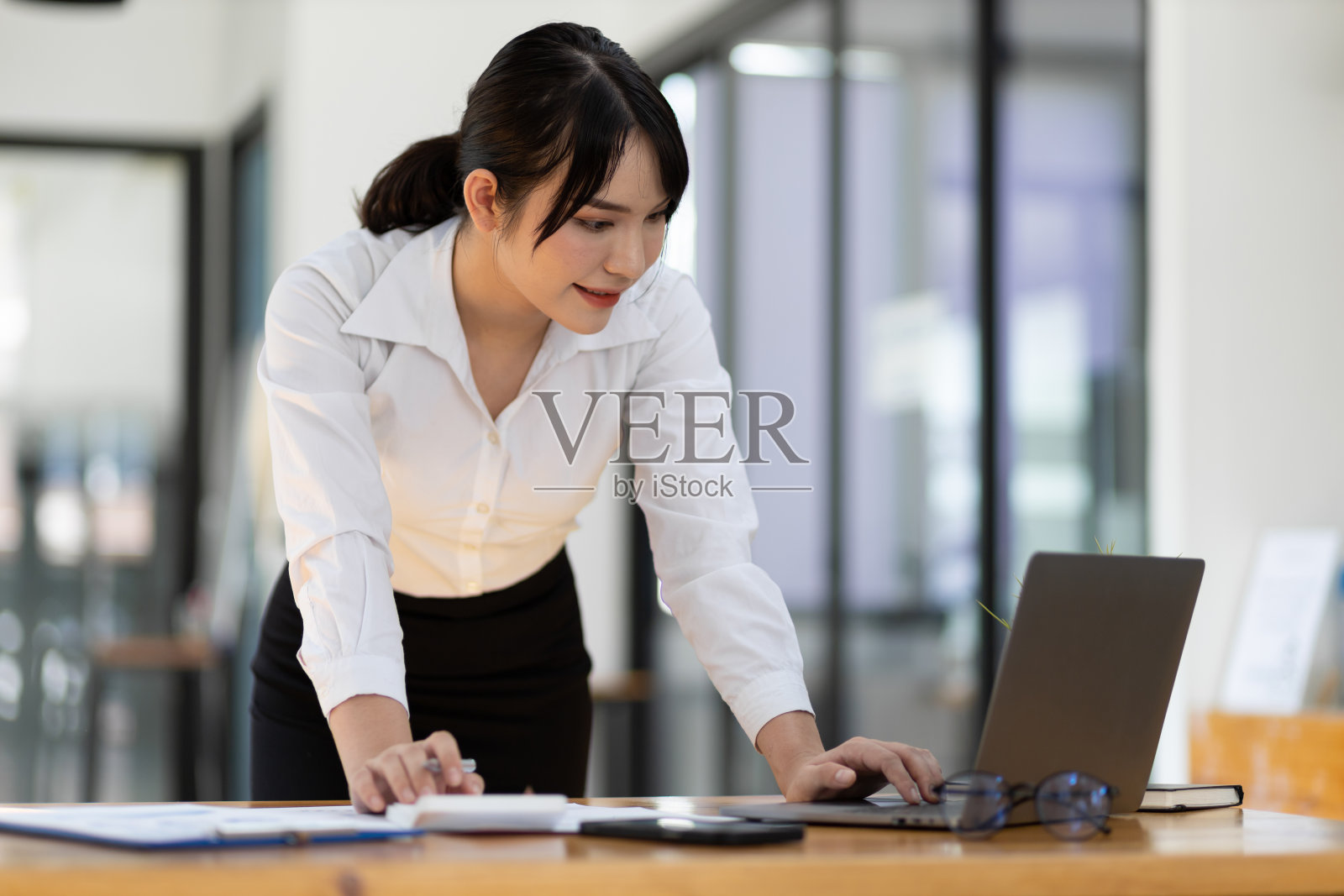 迷人的亚洲女商人用笔记本电脑和办公桌上的文件工作。照片摄影图片