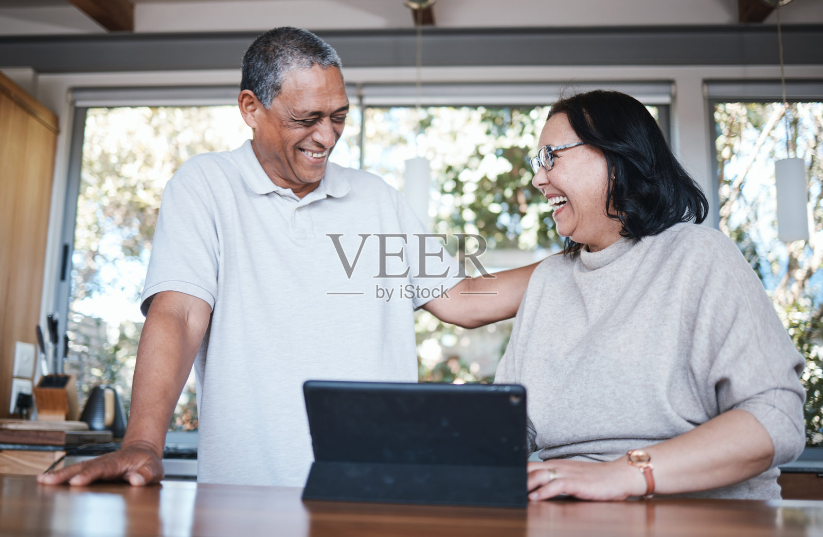 快乐，欢笑和老年夫妇在厨房用数码平板电脑，放松和亲密在他们的家。微笑，大笑和老年人享受退休，笑话和乐趣，而在他们的房子上网浏览照片摄影图片