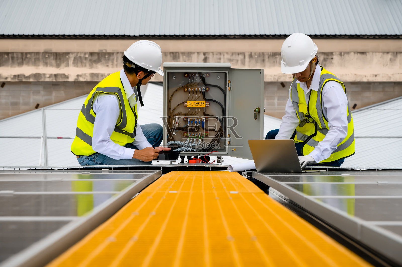 专业工程师和专业技术人员在面板控制中检查电线质量，在平板电脑和笔记本电脑上使用应用程序检查太阳能光伏板的电流容量。照片摄影图片