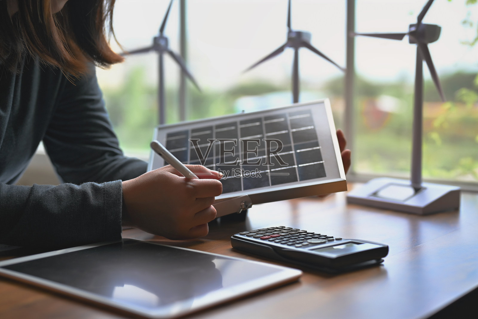 替代能源工程师们拿着太阳能板样品，在办公室里用计算器和平板电脑学习光伏板能量积累的设计和计算。照片摄影图片