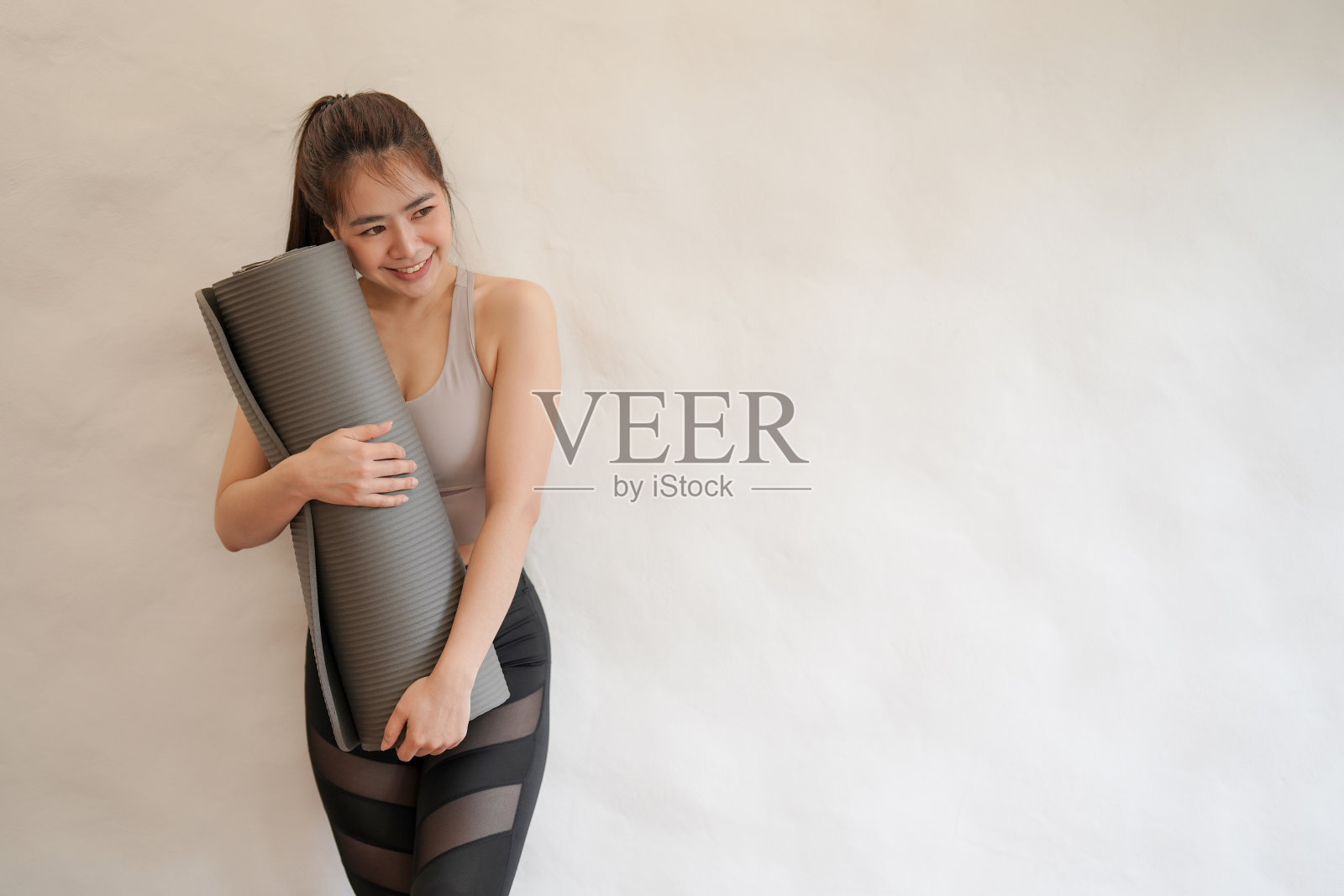 快乐美丽的亚洲女人拿着白色背景的运动服瑜伽垫。照片摄影图片