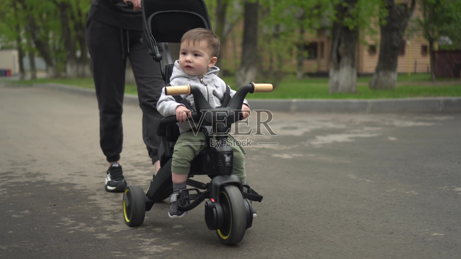 一位年轻的母亲用三轮车抱着一个小孩。两岁男孩骑自行车特写。照片摄影图片