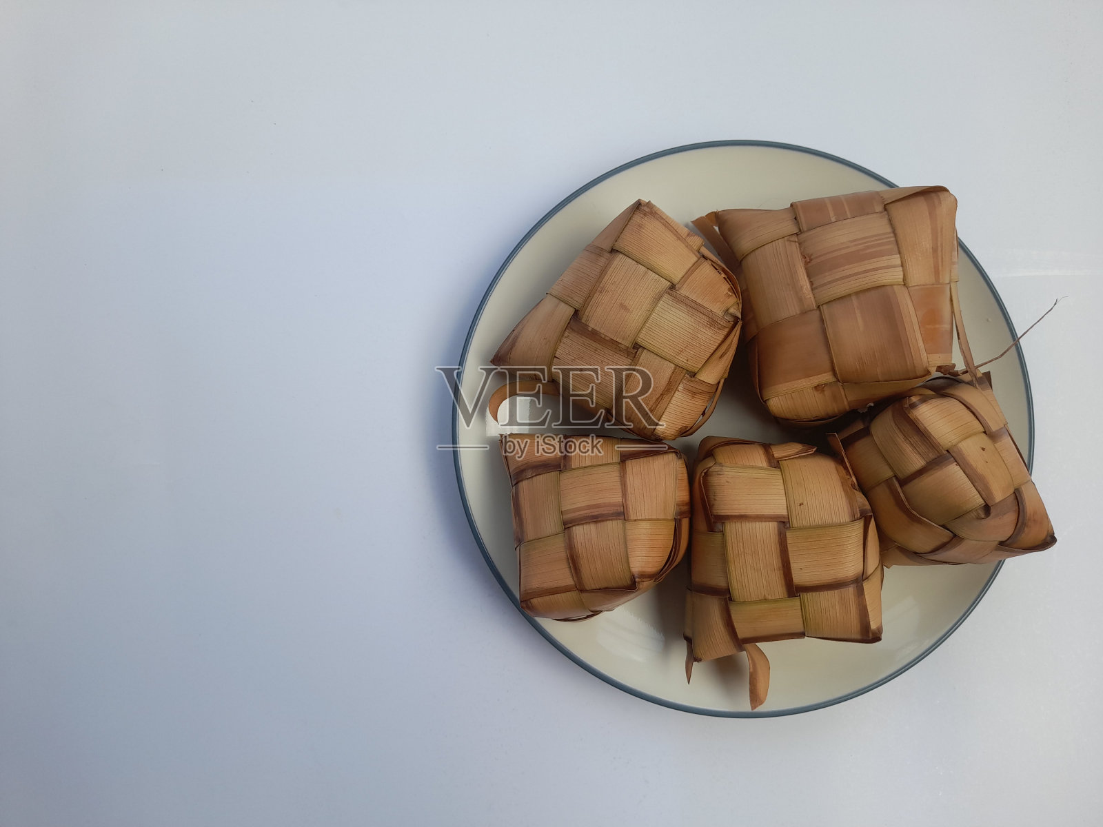 在白色背景下，用椰子叶包裹在盘子里的ketupat食物俯视图照片摄影图片