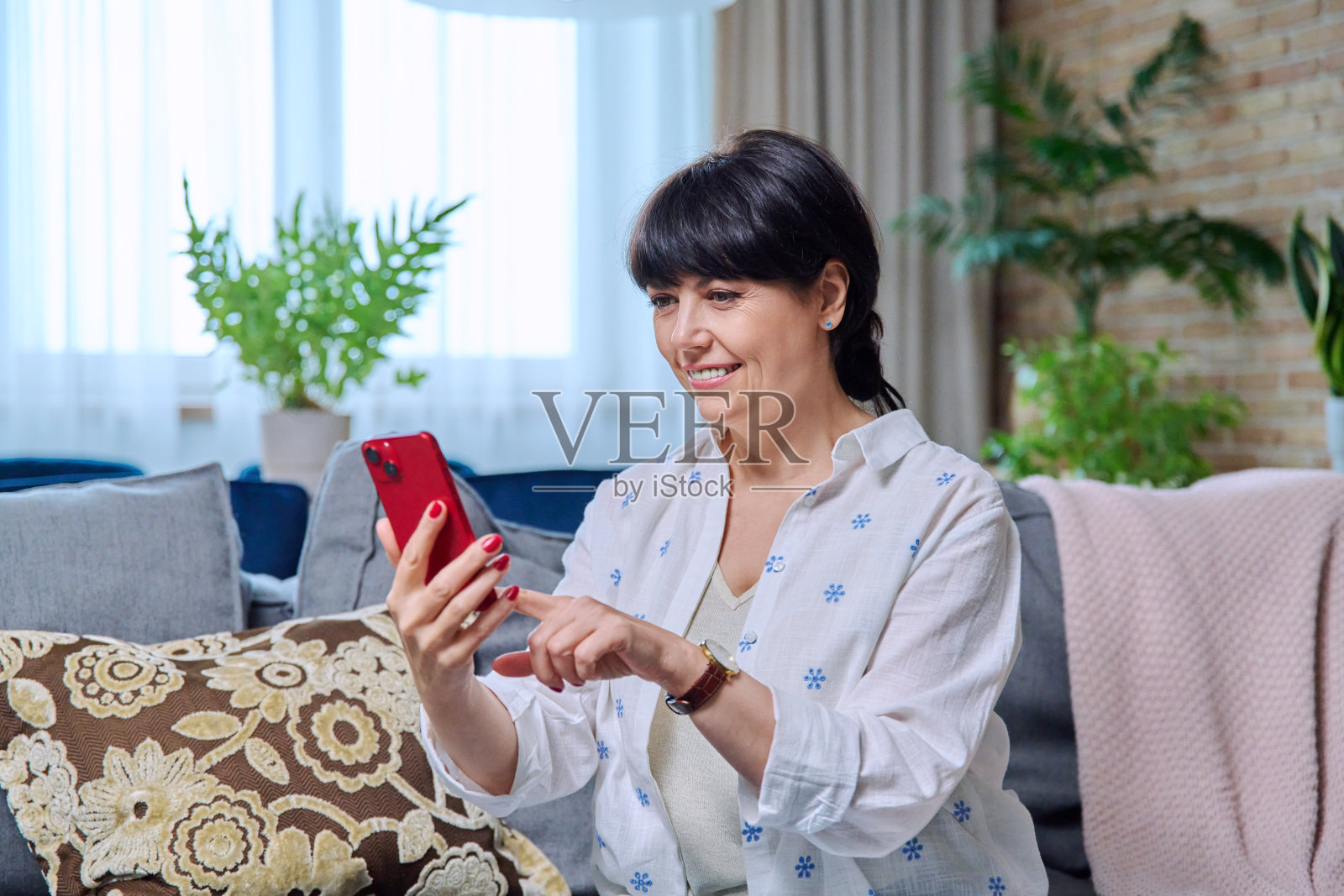 成熟的女人坐在家里的沙发上玩智能手机照片摄影图片