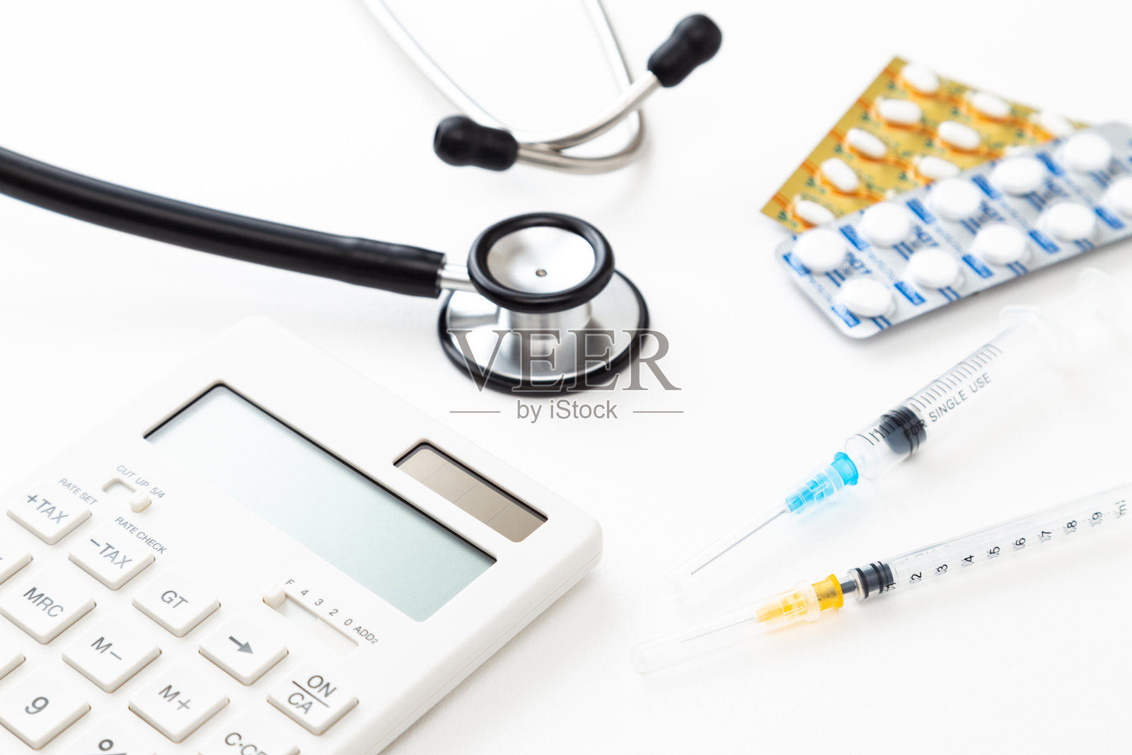 听诊器，注射器，药片和计算器在白色背景。照片摄影图片
