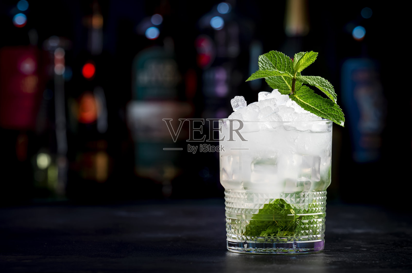 伦敦薄荷混合酒精鸡尾酒，加入干杜松子酒、柠檬汁、糖浆、苏打水、薄荷和冰块。黑色吧台背景，钢筋工具和瓶子照片摄影图片