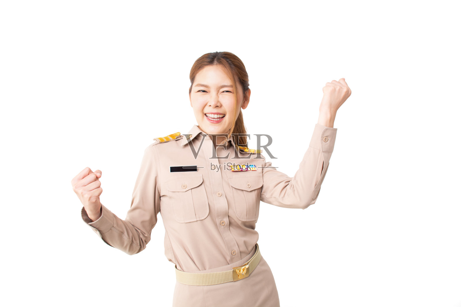 穿着卡其布制服的泰国女政府官员微笑着。美丽的女人在白色的背景上做着胜利者的手势，双臂高高举起。工作理念成功，福利理念认可，信用理念认可。照片摄影图片