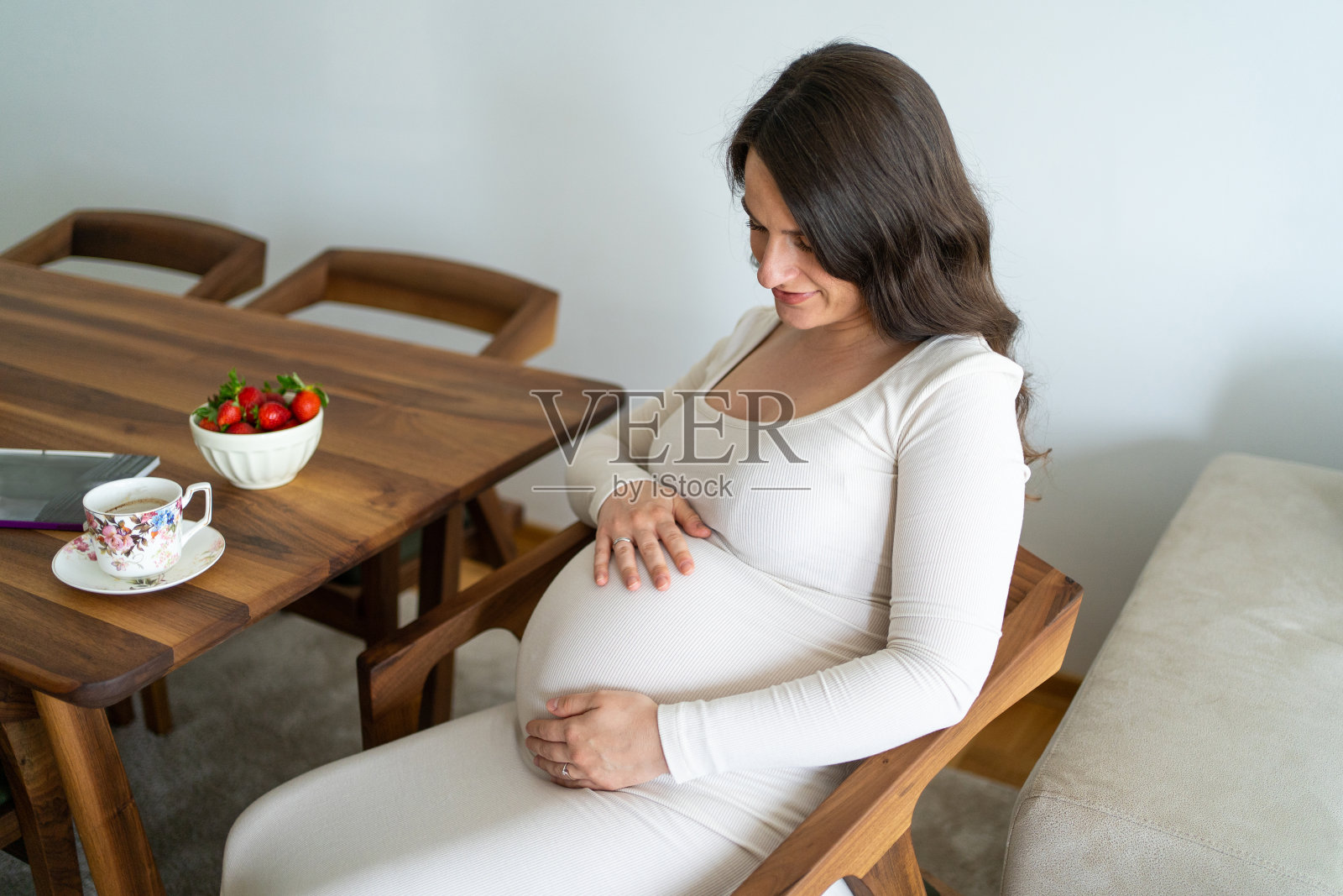 一个孕妇坐在椅子上，抚摸着自己的肚子照片摄影图片