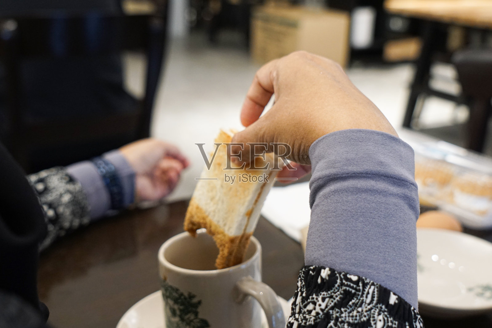 用手将烤面包蘸入咖啡饮料中。照片摄影图片