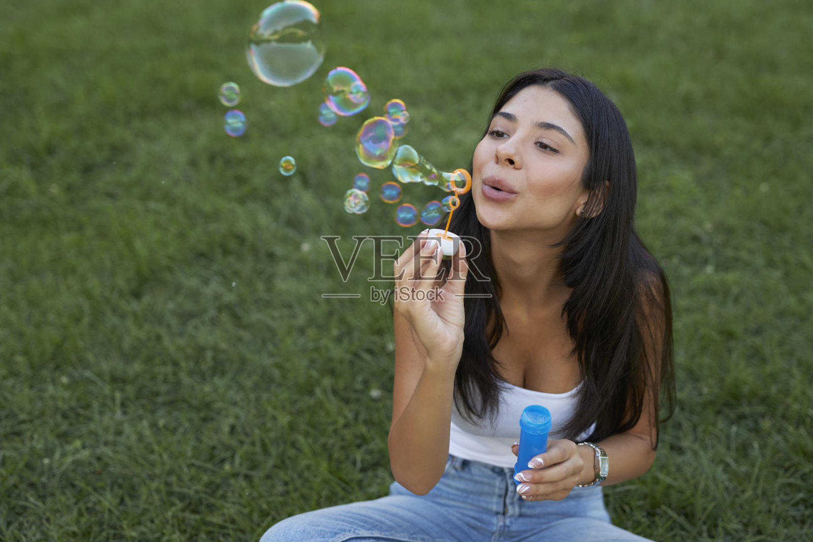 年轻的黑发女郎坐在公园里用泡泡棒照片摄影图片