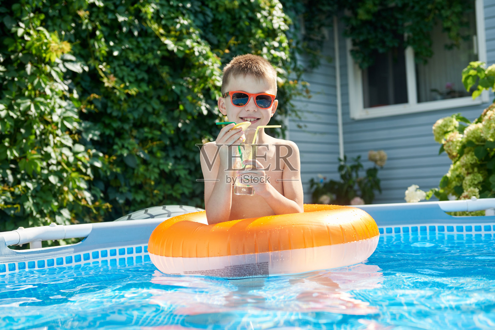 小男孩一边在游泳池游泳一边喝着鸡尾酒照片摄影图片