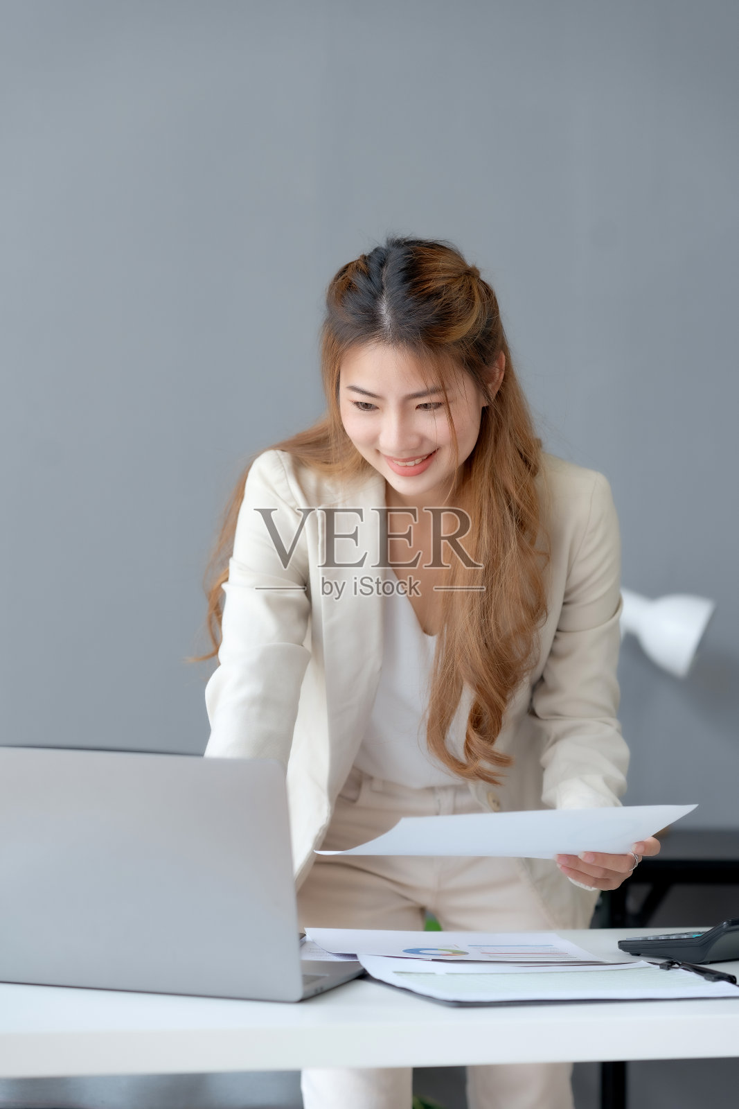 年轻漂亮的商务女性经理或公司工作人员手持会计文件，检查财务数据或营销报告在办公室用笔记本电脑工作。会计咨询一些文件。照片摄影图片