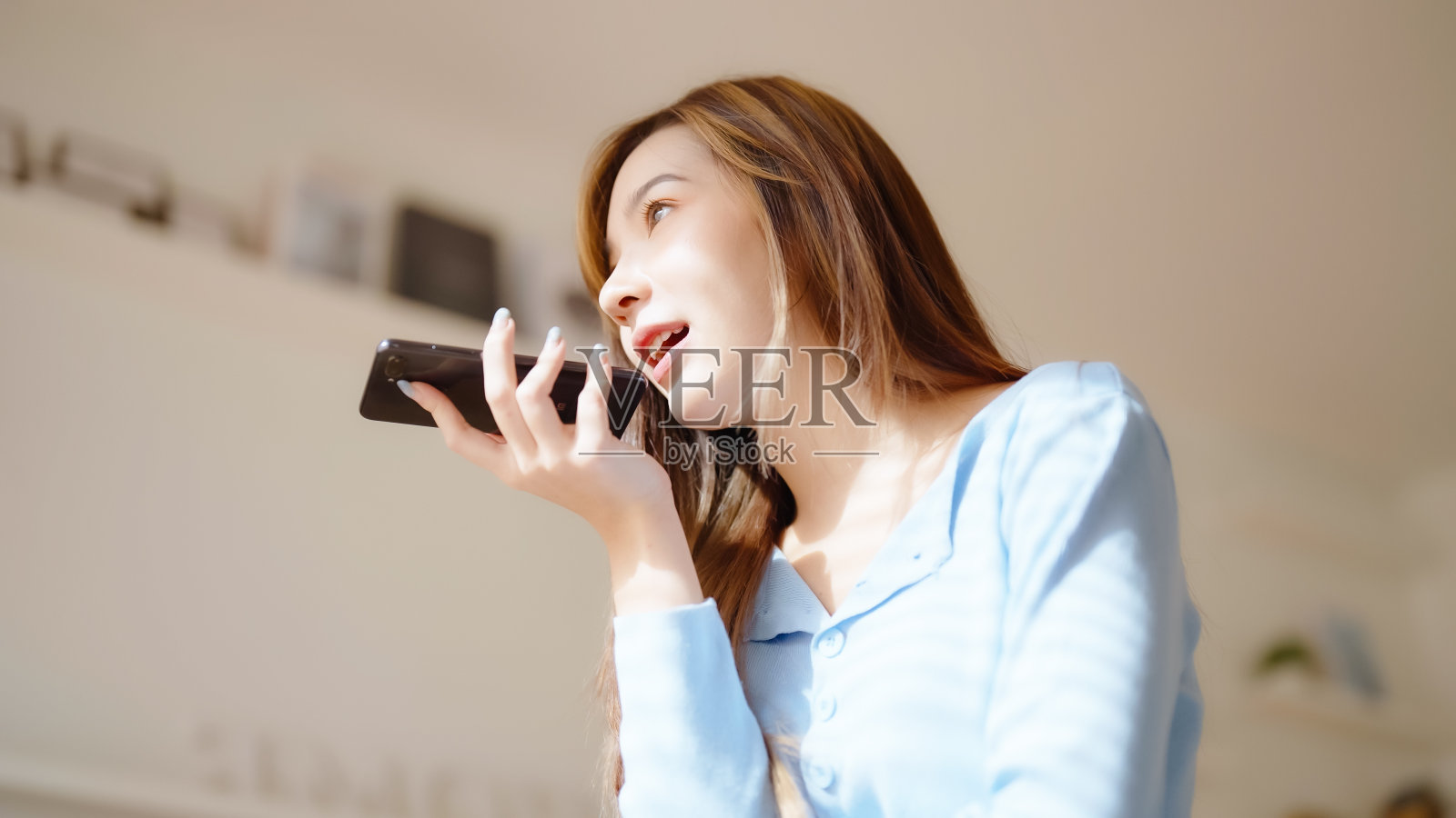 快乐的年轻亚洲妇女在家里讲手机，女青少年坐在沙发上接听电话。亚洲女孩用智能手机聊天照片摄影图片