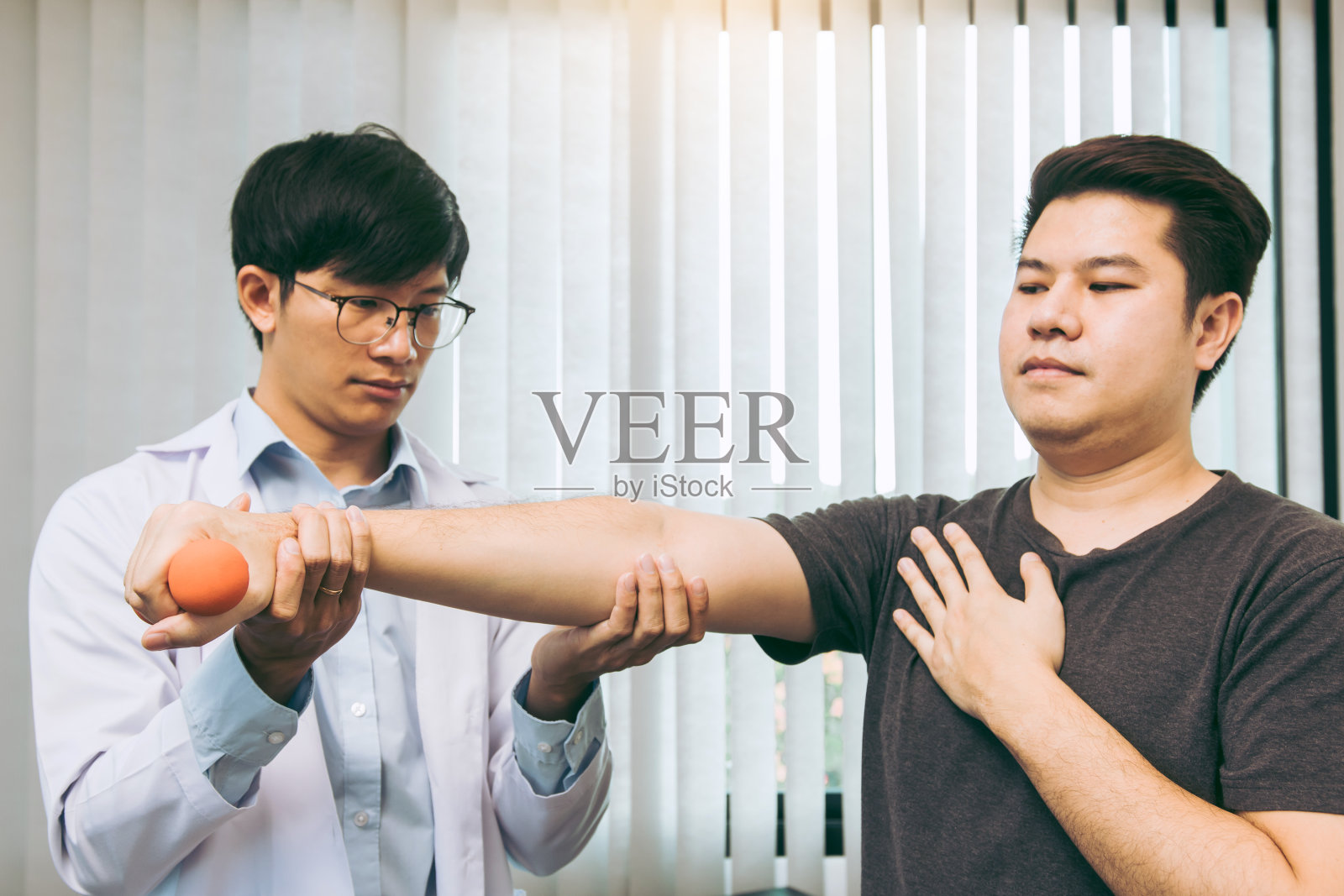 亚洲年轻男性物理治疗师在诊所协助病人进行哑铃练习。照片摄影图片