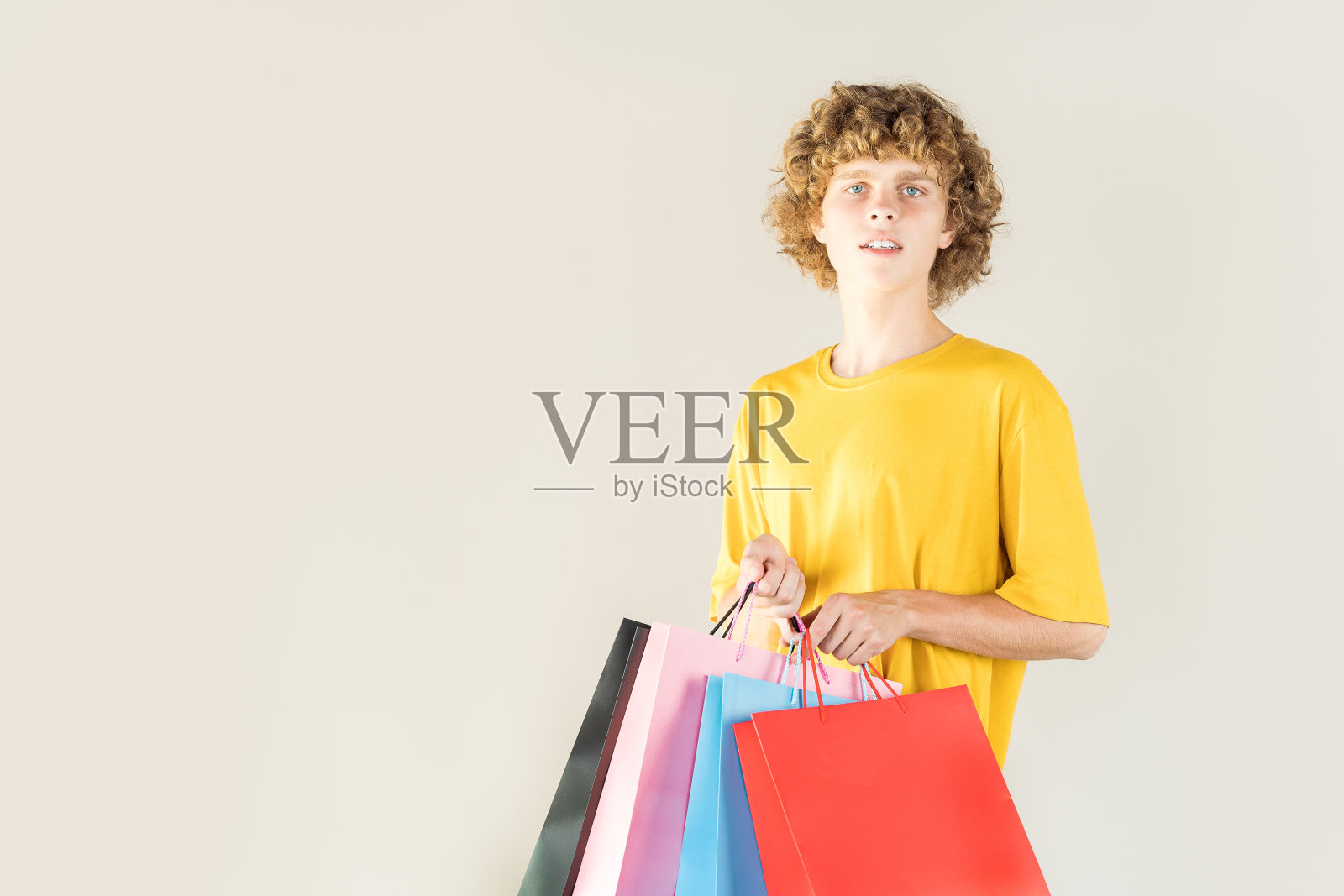 卷曲的年轻人去购物，拿着购物袋在中性背景与复制空间。新收集或销售模型。照片摄影图片