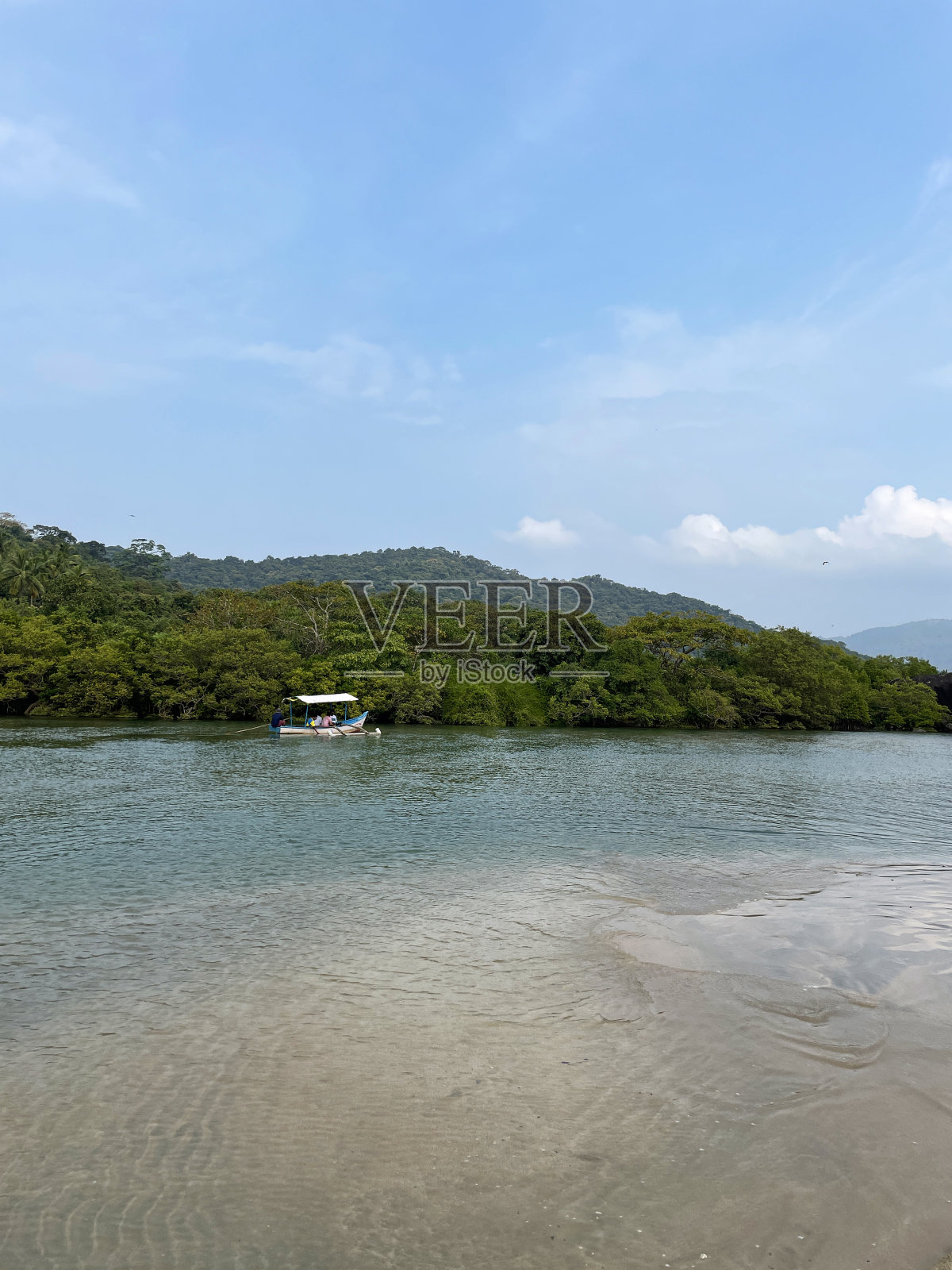 热带岛屿天堂的形象，海浪拍打着海滩，树木繁茂的棕榈树岛，水上的游船，多云的蓝色晴朗的天空，重点在前景照片摄影图片
