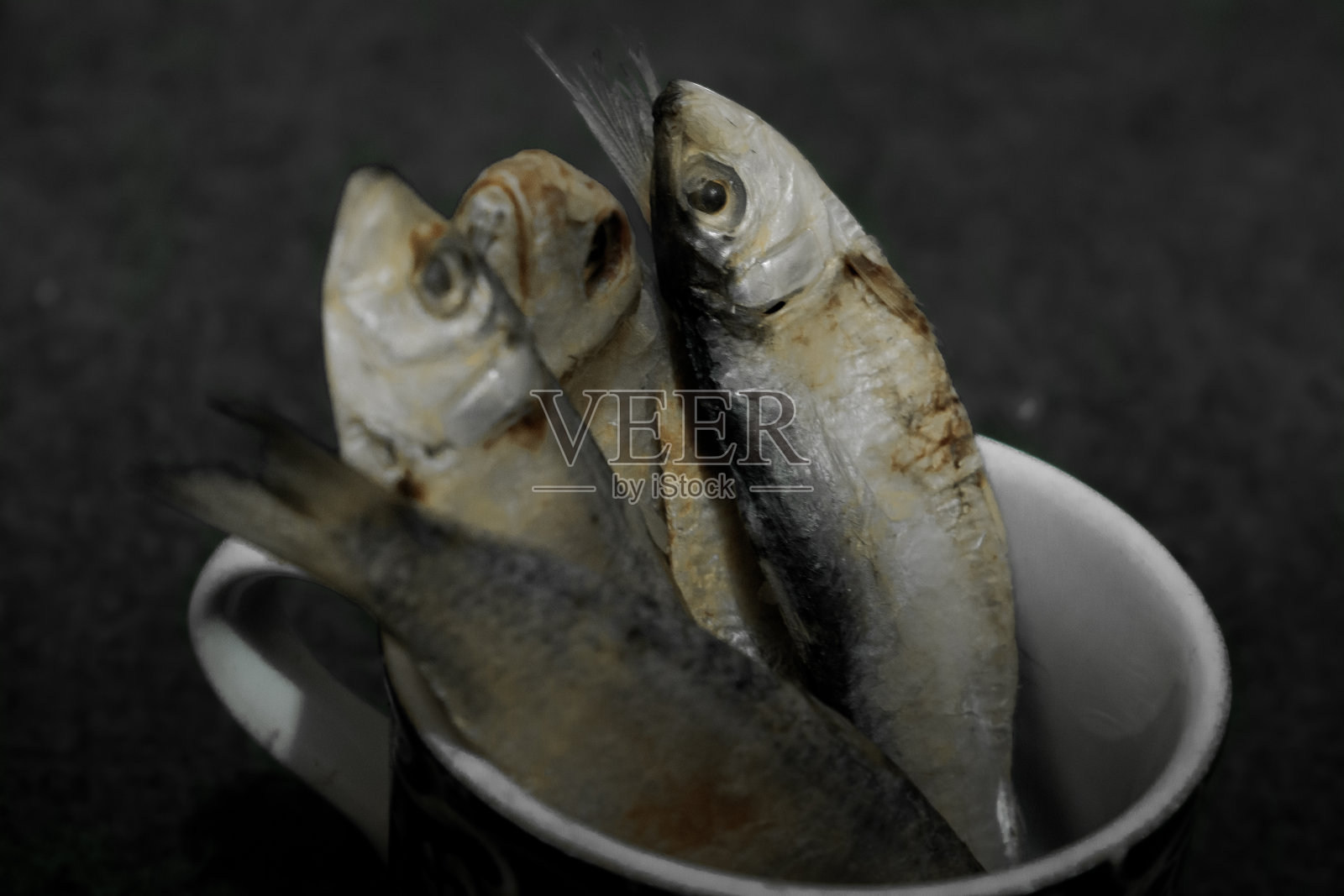 一些咸鱼或干海鱼被装在一个圆形容器里，放在铺着地毯的地板上。照片摄影图片