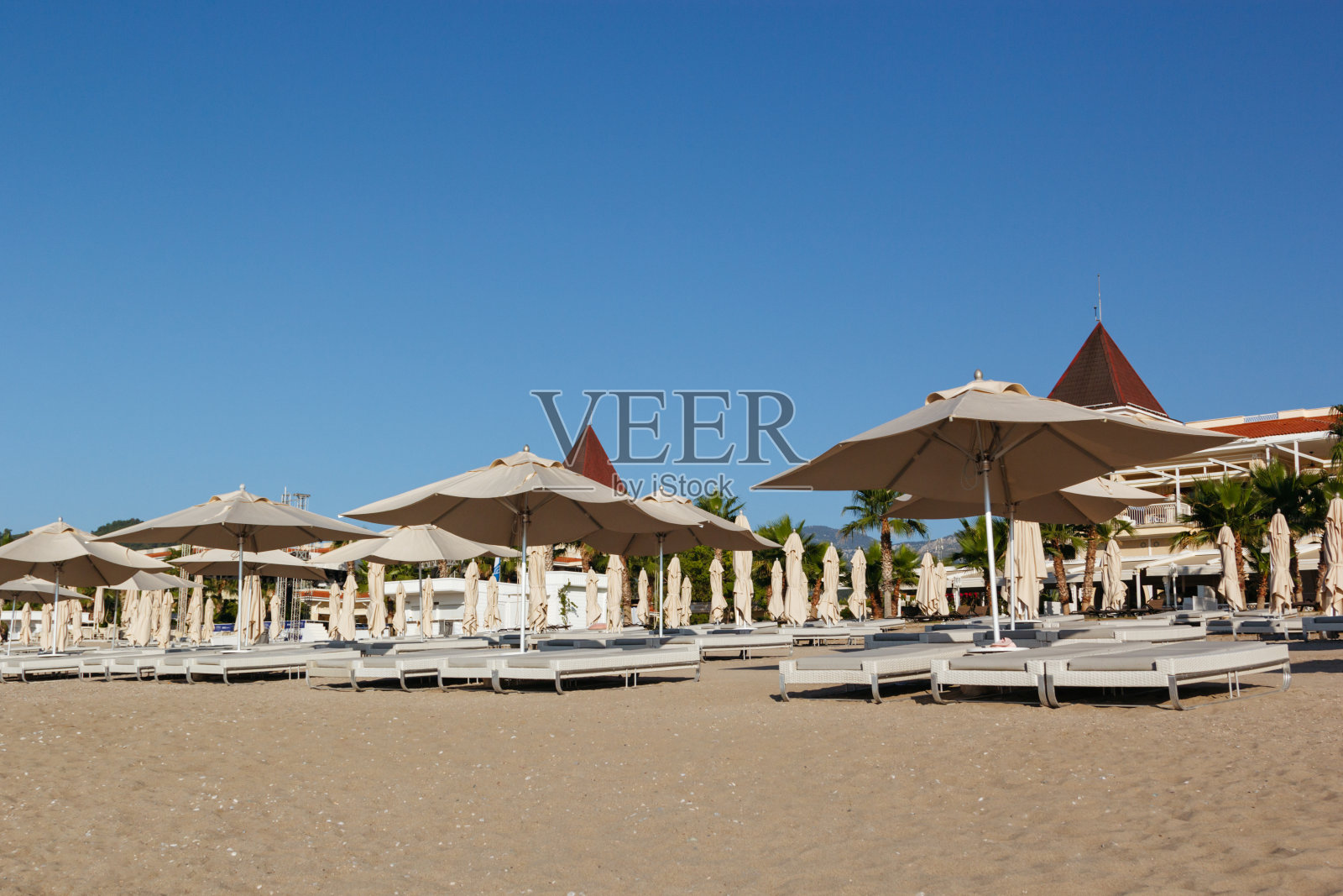 太阳升起时，空旷的海滩上有一排躺椅和遮阳伞等着游客照片摄影图片