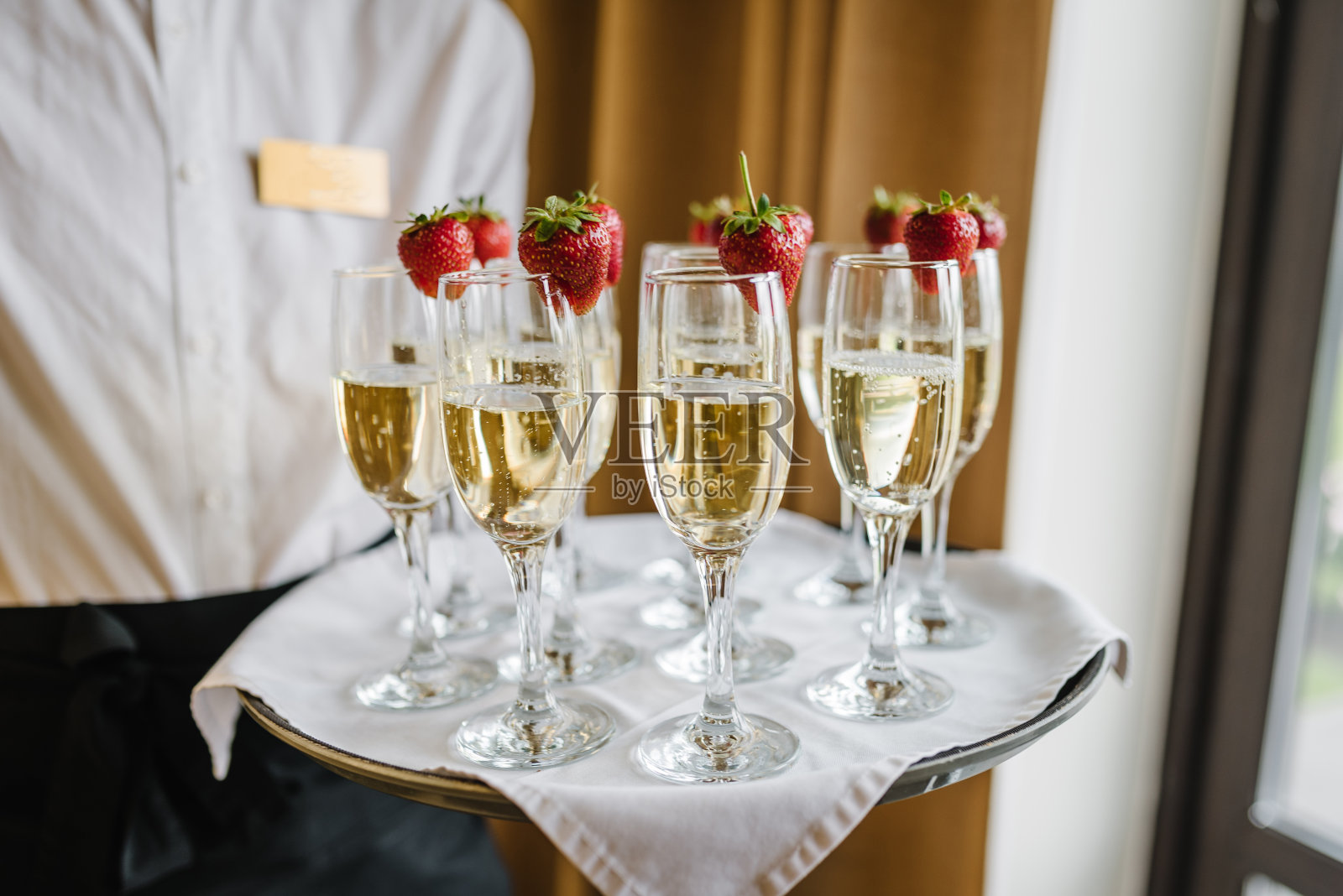 服务员端来了一盘香槟和草莓。派对和节日庆祝的概念。餐饮服务理念。一个女人拿着起泡酒。特写镜头。照片摄影图片