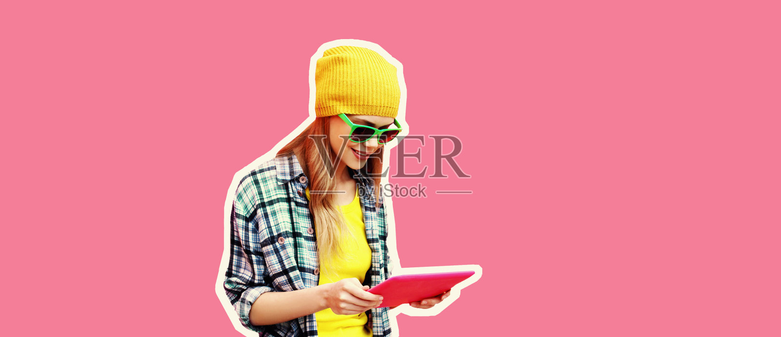 时尚酷的年轻女性模特与平板电脑的肖像穿着彩色的衣服在粉红色的背景，杂志风格照片摄影图片