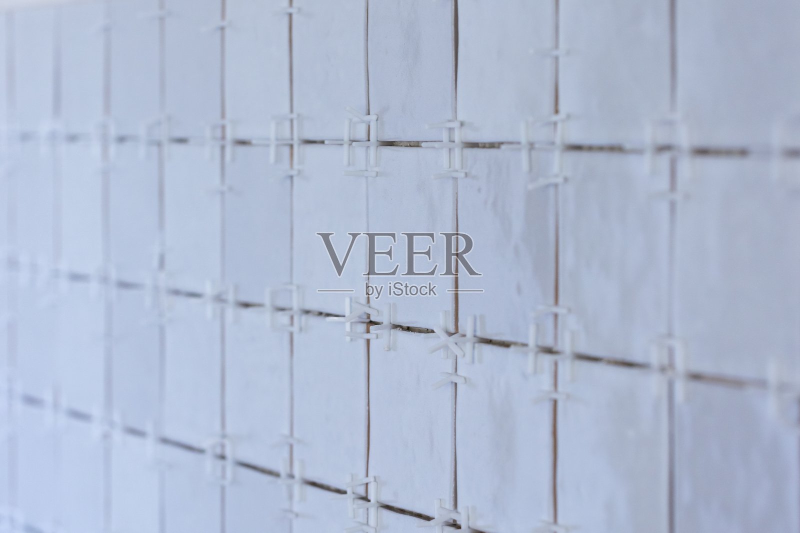 一幅正在施工的瓷砖墙的肖像。墙上正贴着小的矩形瓷砖。瓷砖接缝之间仍然有白色的塑料接缝垫片。照片摄影图片