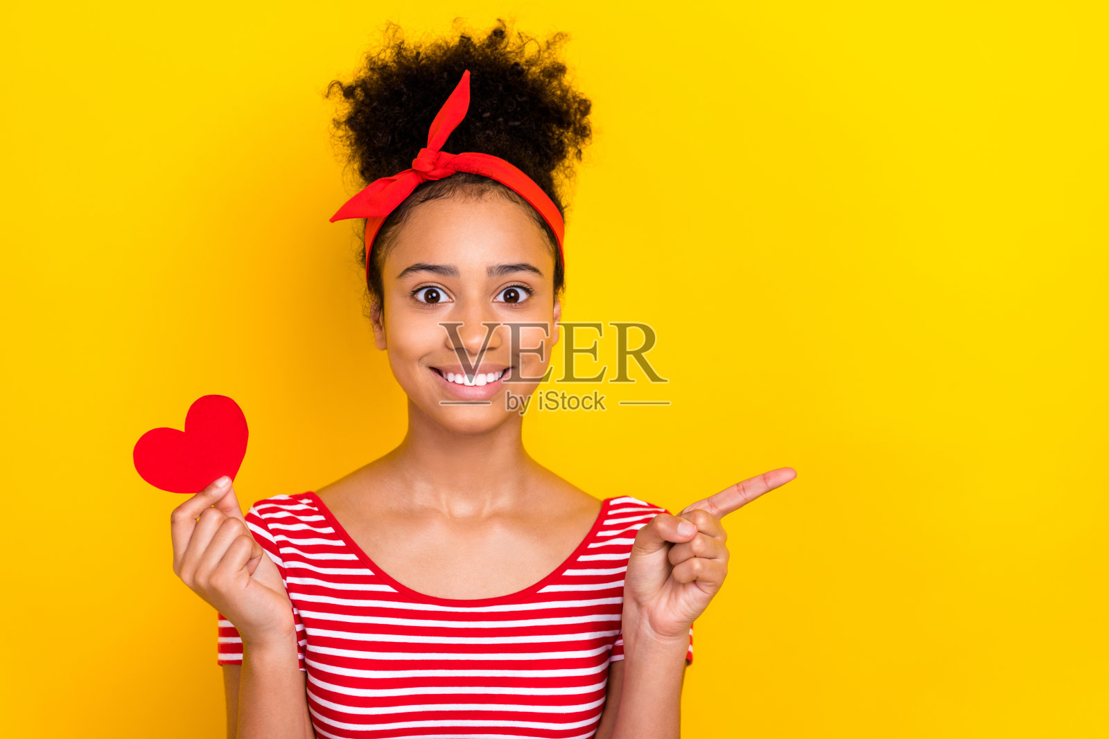 照片中漂亮闪亮的女士穿着条纹红色t恤，心牌上升，手指指向空白空间，孤立的黄色背景照片摄影图片