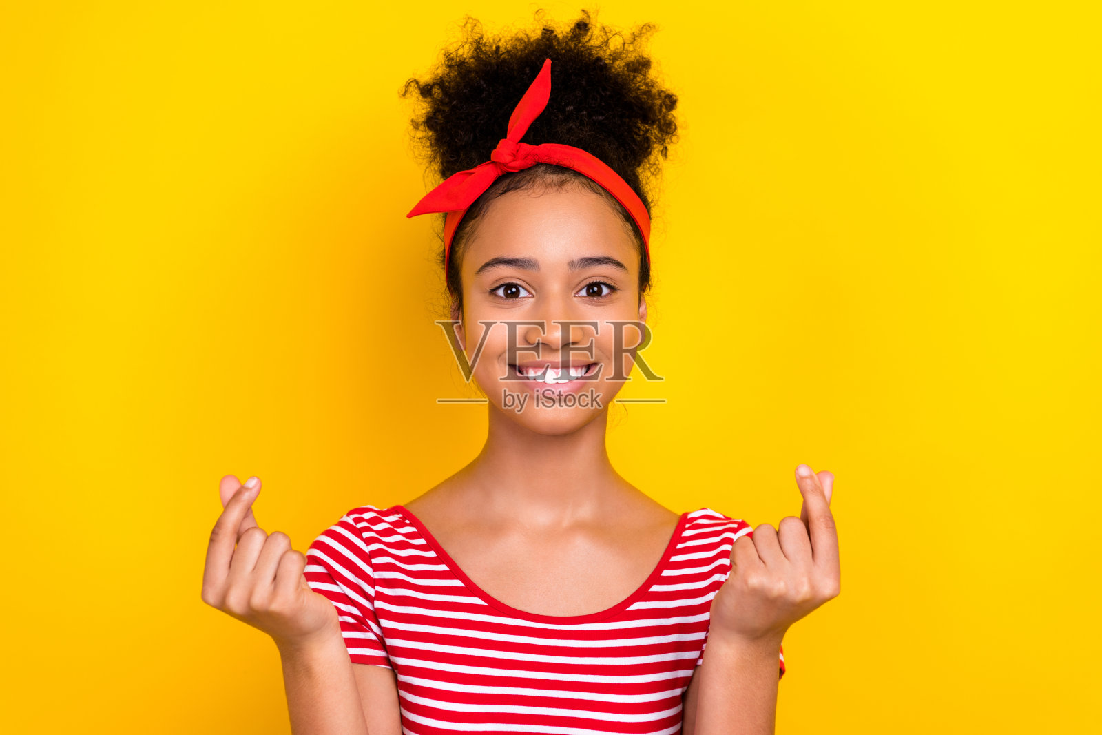 照片中，穿着红色条纹t恤的开朗女士微笑着展示了韩国人的心形手势，孤立的黄色背景照片摄影图片