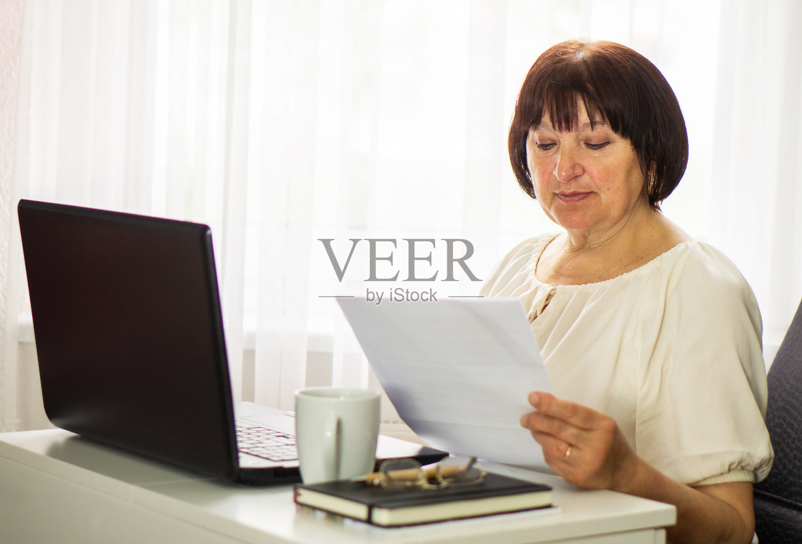 中年老年妇女坐在那里拿着笔记本电脑和文件。照片摄影图片