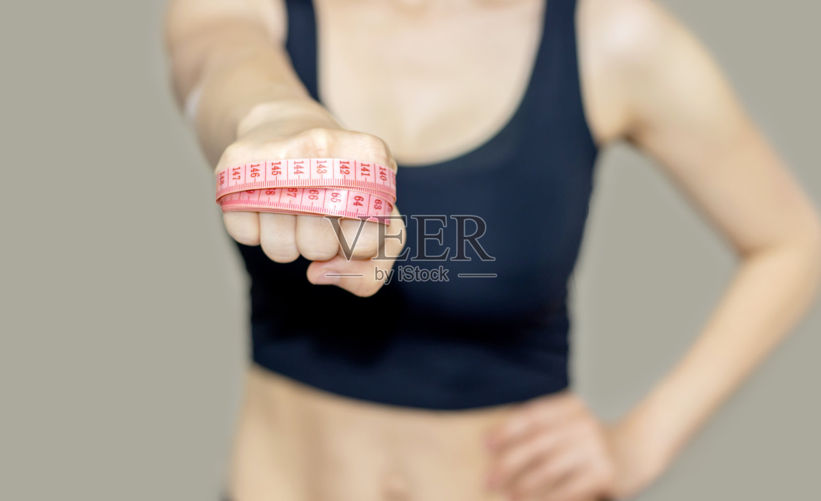 女人双手向前伸展，把卷尺紧紧地绕在手上。踢拳击的位置。对抗多余的脂肪，减肥的概念。健身，瘦身，节食。女孩露出训练有素的腹部。照片摄影图片