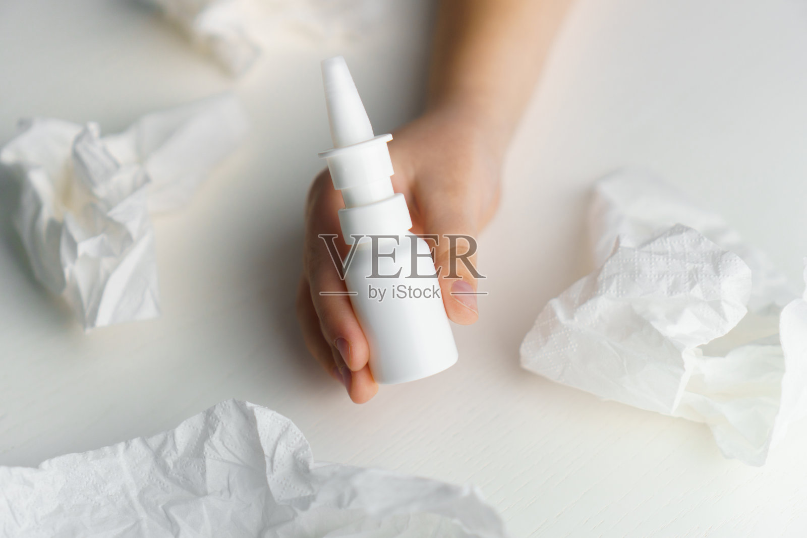 孩子手里拿着药瓶，鼻子喷雾剂放在白色的桌子上用纸巾。治疗流鼻涕照片摄影图片