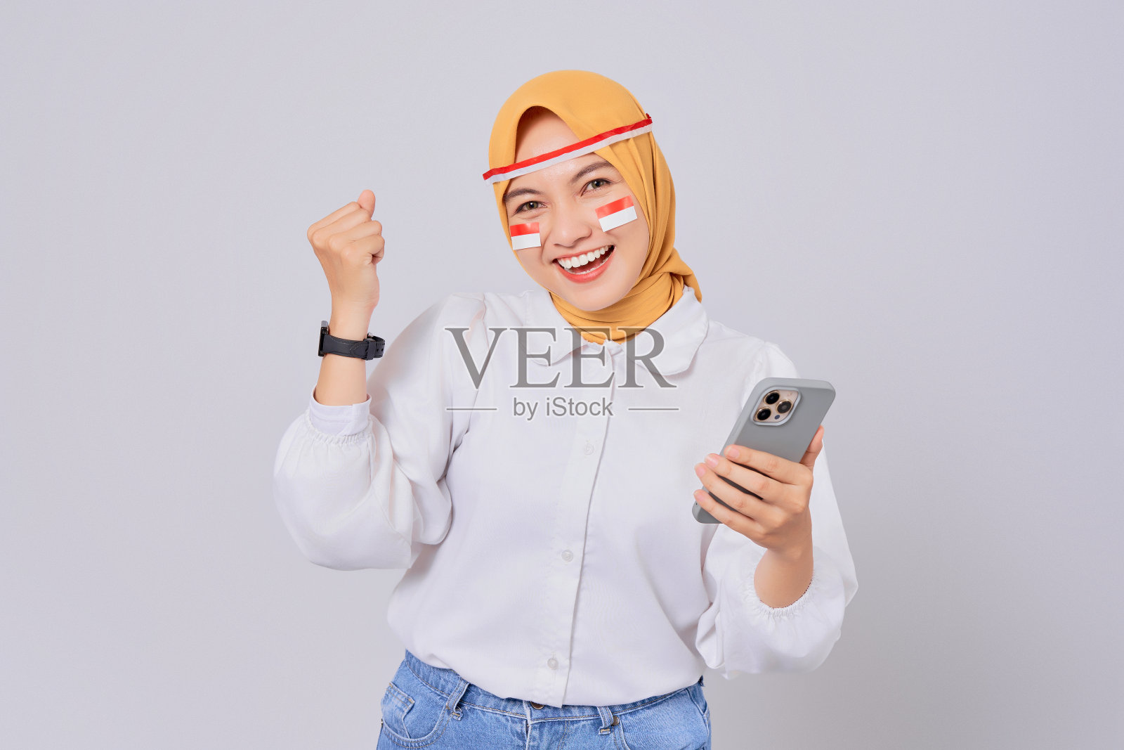 8月17日，兴奋的年轻亚洲穆斯林妇女戴着头巾，用智能手机庆祝印度尼西亚独立日照片摄影图片