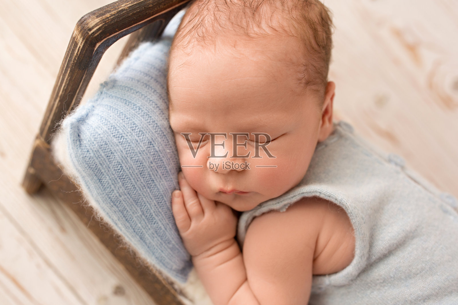 一个可爱的新生男孩在生命的最初几天穿着蓝色的工装裤睡在棕色的木床上。蓝色的头枕。在浅色的木制背景下。照片摄影图片